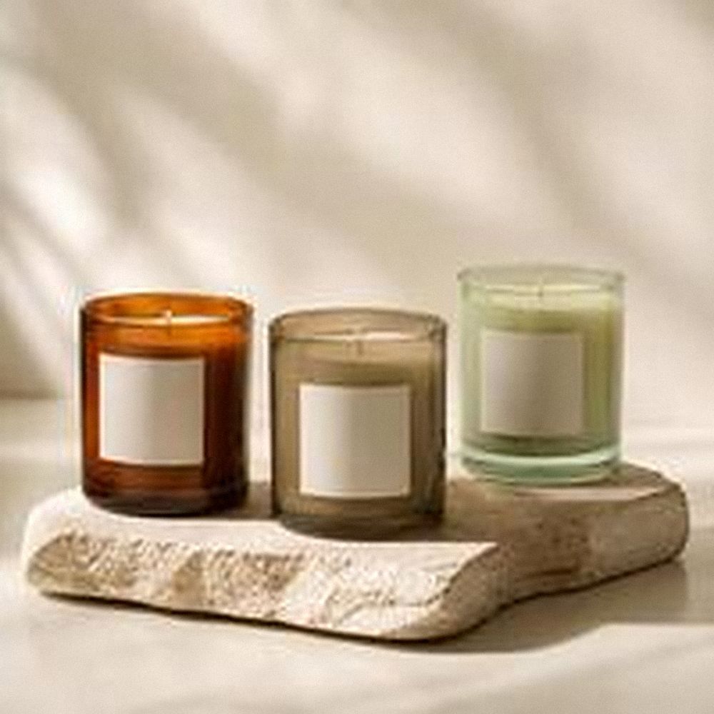 Tres velas de vidrio en tonos ámbar, taupe y verde claro sobre una losa de piedra